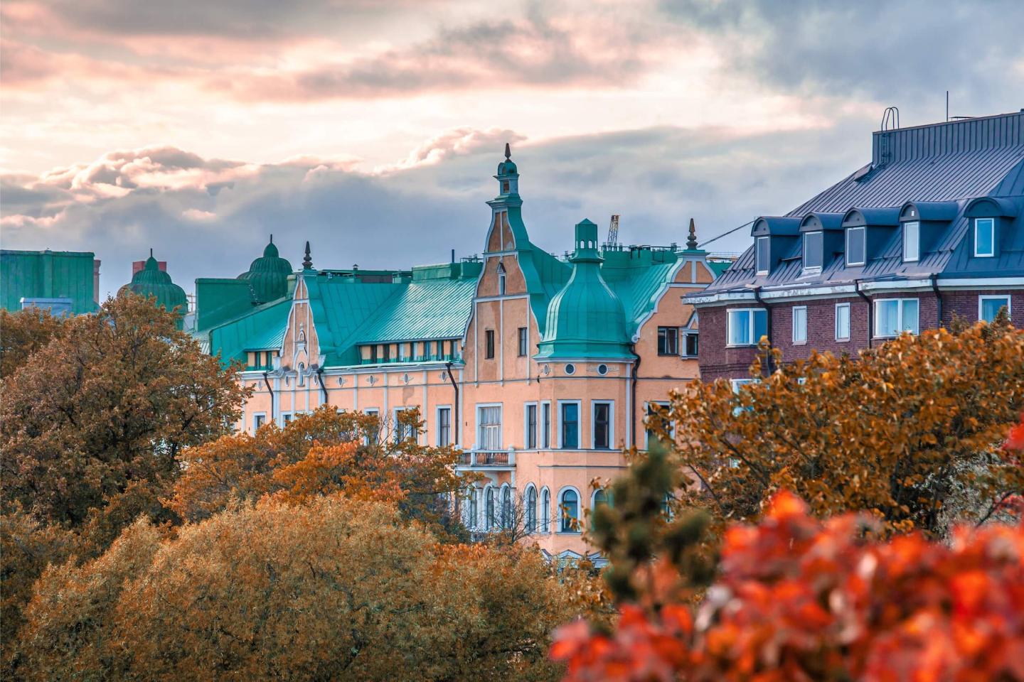 Colorful historic Finland buildings with green rooftops rise above autumn trees under a cloudy sky, creating a picturesque cityscape scene.